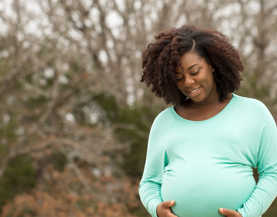 Black pregnant surrogate in mint-green shirt holding her belly, part of screening surrogates