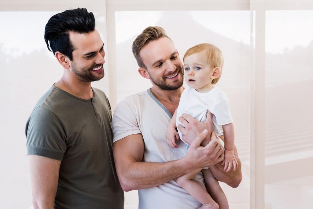 Smiling gay couple with child who underwent surrogacy