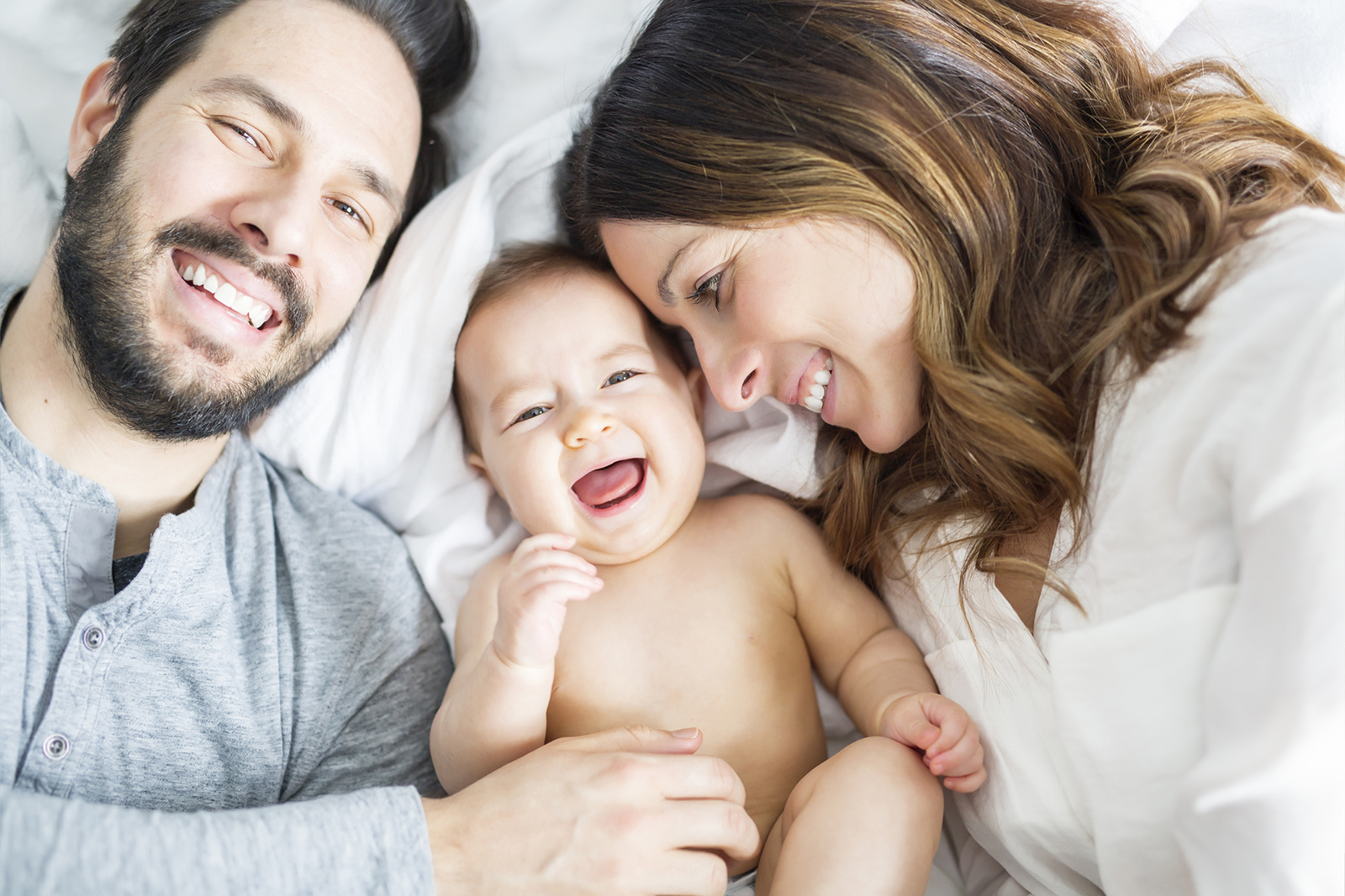 Mother and father via surrogacy with their baby on a bed